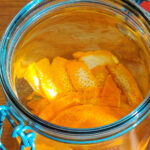Orangenschale in ein Glas legen und mit dem Alkohol bedecken